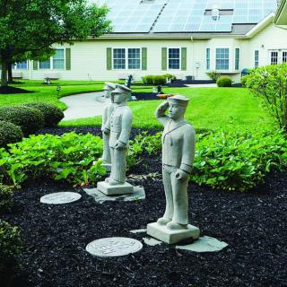 Two statues stand in a landscaped garden with a building in the background.