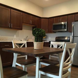 A modern kitchen with dark wood cabinets, a central dining table, and stainless steel appliances.