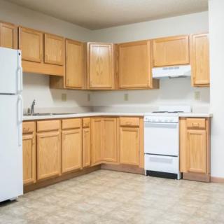 An empty apartment kitchen featuring wooden cabinets, a refrigerator, and a stove.