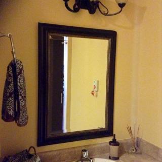 A bathroom with a mirror above the sink, featuring a towel hook and light fixture.