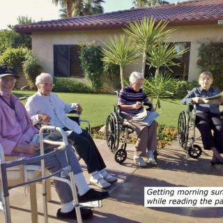 Seniors enjoying the morning sun while reading in wheelchairs.