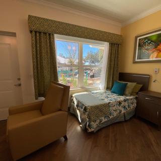 A well-lit hospital room with a bed, chair, and a large window with curtains.