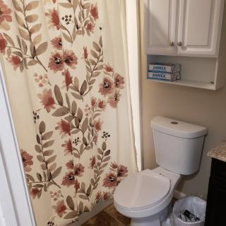 A small bathroom with a floral shower curtain and white cabinetry.