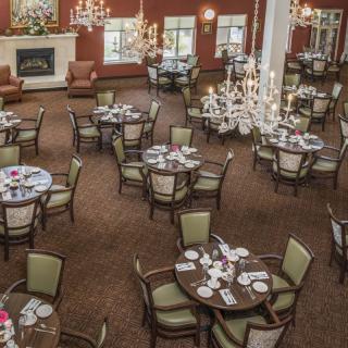 An elegant dining room with multiple round tables neatly set for guests, featuring chandeliers and a warm decor.