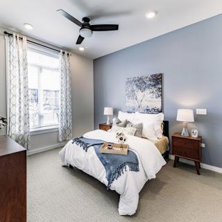 A modern bedroom with a cozy bed, stylish decor, and natural light from a large window.