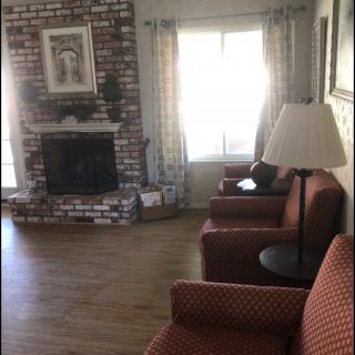 A cozy living room with a brick fireplace, comfortable armchairs, and a large window letting in natural light.