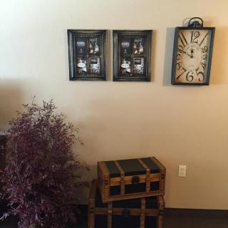Cozy corner with a wall clock, decorative frames, an indoor plant, and a wooden chest.