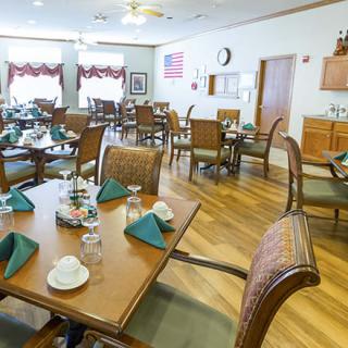 A neatly arranged dining room with tables set for service, featuring wooden flooring and natural lighting.