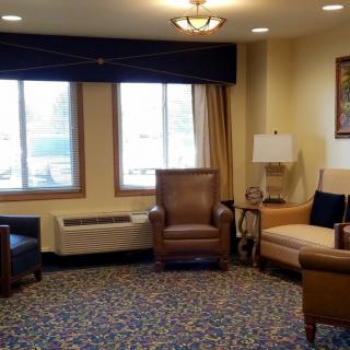 A cozy living room with various armchairs and a lamp, featuring large windows that let in natural light.