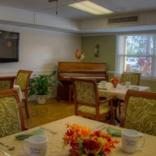 A cozy dining room with a piano, television, and elegantly set tables adorned with flowers.