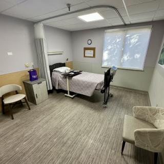 A clean and organized hospital room equipped with a bed, seating area, and natural light.