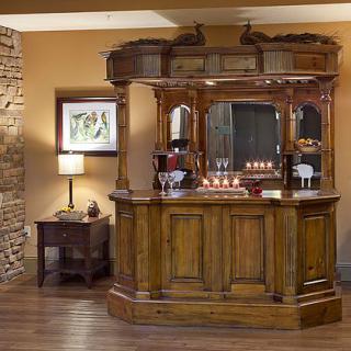 A vintage-style wooden home bar set against a warm-toned interior with a side table and lamp.