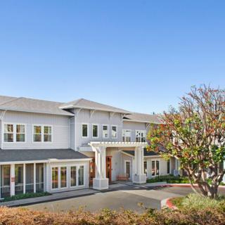 A large residential house with a spacious entrance and surrounding trees under a clear sky.