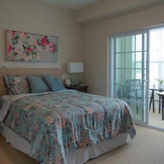 A cozy bedroom with a floral bedspread, artwork on the wall, and access to a balcony through sliding glass doors.