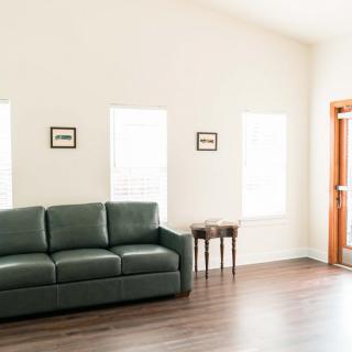A minimalist living room with a green sofa, wooden flooring, and ample natural light.