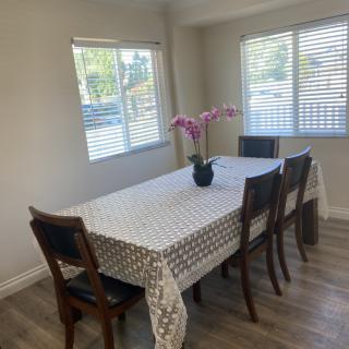 A dining room with a table covered by a tablecloth, surrounded by chairs and decorated with an orchid in a flower vase.