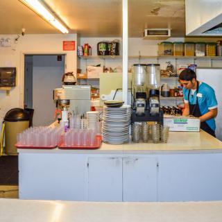 A worker in a restaurant kitchen preparing drinks and organizing dishes.