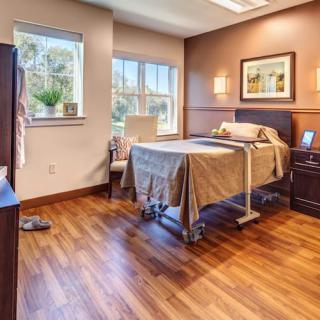 A well-lit hospital room featuring a single bed and wooden flooring.