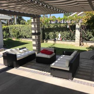 A sunny patio with modern outdoor furniture and a pergola, overlooking a well-maintained garden.