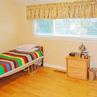 A simple bedroom with a single bed featuring a colorful blanket, next to a nightstand and a window with curtains.