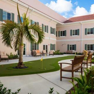 A tranquil courtyard featuring benches and a palm tree, surrounded by a light-colored building under a clear blue sky.
