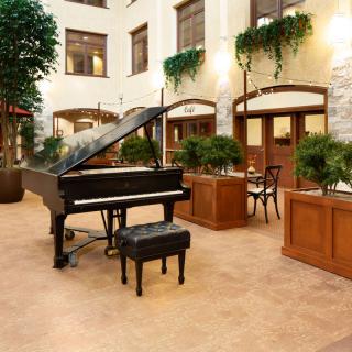 A spacious lobby featuring a grand piano and seating area surrounded by lush greenery.