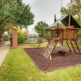 A children's playground with a swing set and slide, adjacent to a gazebo in a grassy outdoor park.