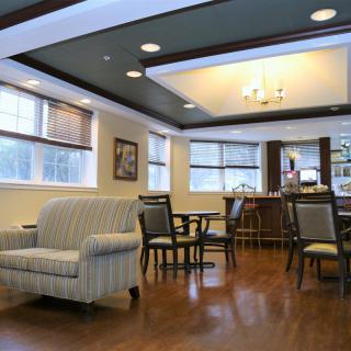 A cozy lounge area with comfortable seating and a chandelier, featuring wooden floors and large windows.