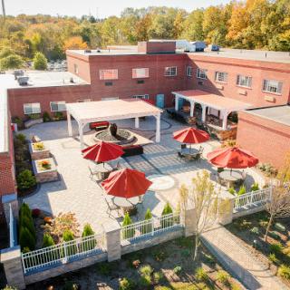 Aerial view of a modern building with a landscaped patio featuring red umbrellas, set against a backdrop of autumn foliage.