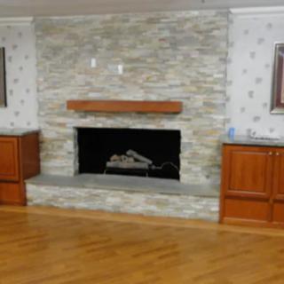 A cozy living room features a stone fireplace with a wooden mantle, flanked by built-in cabinets on a hardwood floor.