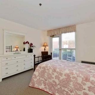 A cozy bedroom with a floral bedspread, a white dresser with a mirror, and soft lighting from a lamp by the window.