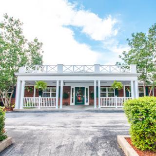 A charming building with a welcoming front entrance, surrounded by lush greenery under a bright blue sky.
