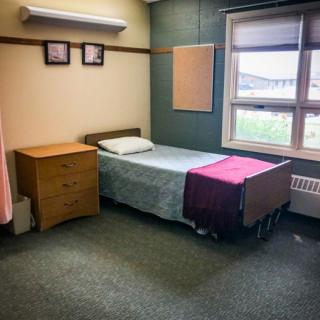 A simple hospital room featuring a single bed, a nightstand, and a window.