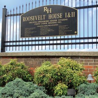 Sign for Roosevelt House I & II mounted on a fence above landscaped plants.