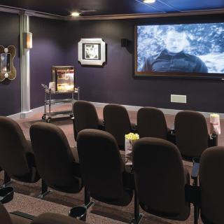 A cozy home theater setup with rows of seating and a large screen displaying a film.