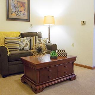 A cozy living room with a sofa adorned with cushions, a wooden coffee table, and a standing lamp, complemented by wall art.