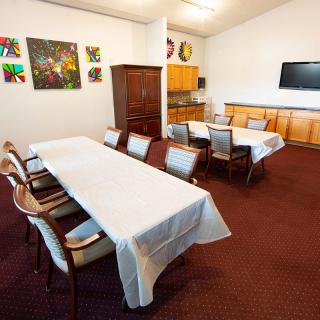 A well-equipped conference room featuring tables covered with white cloths, chairs, a television, artwork on the walls, and a carpeted floor.