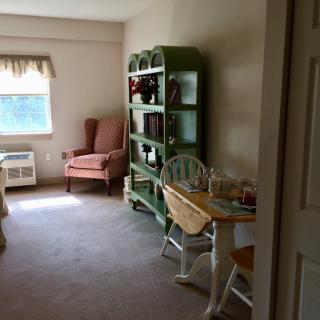 A cozy living area featuring an armchair, bookshelf, and small dining table by the window.