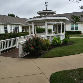 A charming gazebo surrounded by a garden with a paved pathway leading to it.