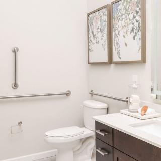 A modern bathroom with accessibility features, including handrails near the toilet and sleek decor.