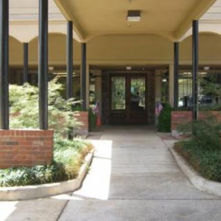The entrance to a building with a covered walkway and landscaped surroundings.