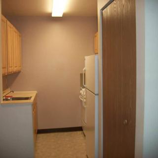 A small kitchen with wooden cabinets, a refrigerator, and a sink in an apartment.