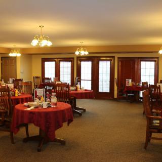 An empty dining room with tables and chairs set with red tablecloths.