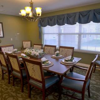 A neatly arranged dining room with a large table set for a meal, featuring elegant chairs, a chandelier, and natural light coming through the window.