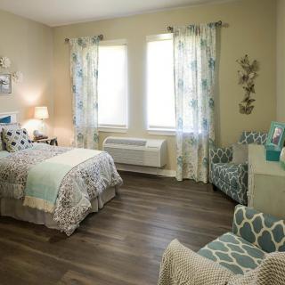 A cozy bedroom featuring stylish decor with a bed, chairs, and large windows allowing natural light.