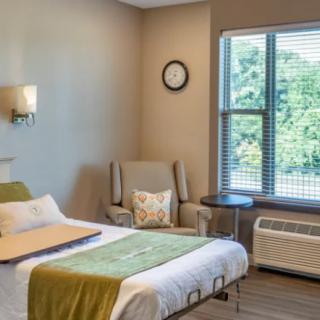 A cozy and minimalist bedroom with a single bed, armchair, and large window allowing natural light to fill the space.