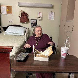 An elderly woman seated at a table in a nursing home, enjoying her meal.