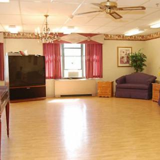 A spacious room with wooden flooring, a sofa, a television, and red curtains by the window.
