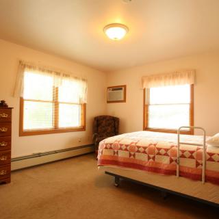 A cozy bedroom with a bed, dresser, and armchair by the window.