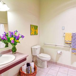 A bright and clean bathroom with colorful decor, featuring a toilet, sink with fresh flowers, and neatly arranged towels.